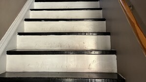 Una escalera con peldaños blancos y bordes negros, barandillas de madera y de metal.