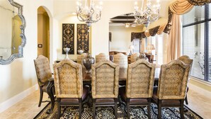 Ein Esszimmer mit einem großen Tisch, verzierten Stühlen, Kronleuchtern und einem gemusterten Teppich.