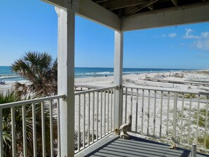 Uitzicht op een strand vanaf een overdekt terras met een balustrade, met palmbomen en een zandstrand op de achtergrond.