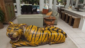 Un salon comprenant une grande statue de tigre, un canapé, une table basse et un coin cuisine avec des tabourets.