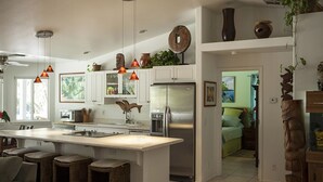 Une cuisine moderne dotée d’un îlot central, d’appareils électroménagers en acier inoxydable et de luminaires suspendus.