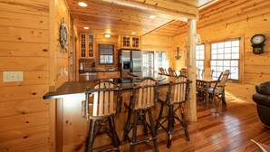 A wooden cabin interior with a kitchen, dining area, and a living room.