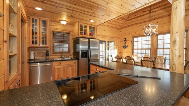 A modern kitchen with wooden cabinetry, a stainless steel refrigerator, a dishwasher, and a granite countertop.