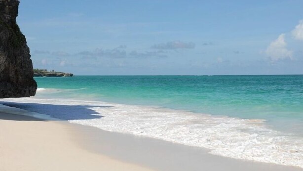 A beach with clear turquoise water, white sand, and a large rock formation on the left. - Your Relaxing Tropical Getaway Near Crane Resort - 3 bedroom (The Crane)