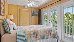 A bedroom with a bed, a ceiling fan, a window with a view of greenery, and a door. - Family Retreat Ocean front pool (Cudjoe Key)