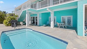 A poolside area with a pool, outdoor seating, and a building with a balcony. - Family Retreat Ocean front pool (Cudjoe Key)
