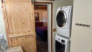 A compact laundry room with a washing machine, dryer, and a wooden door leading to a bedroom. - Lakefront Retreat on 14+ Acres | Unforgettable Lake Getaway (Little Elm)