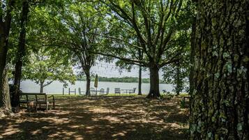 Un parc avec un banc, des tables et des chaises, le tout installé sous les arbres, près d’un lac.