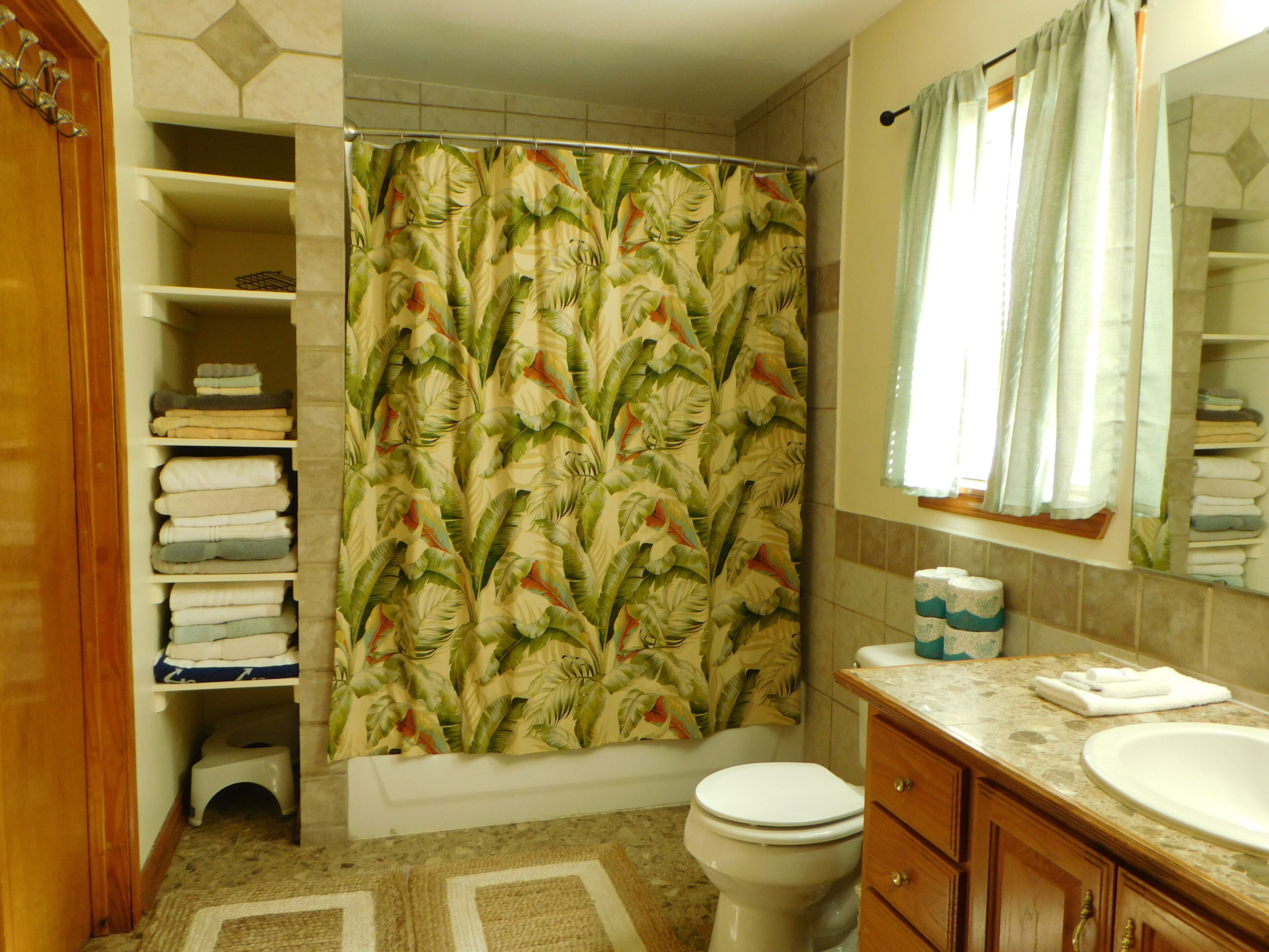 Une salle de bain avec un rideau de douche, des toilettes, un lavabo et des étagères avec des serviettes.