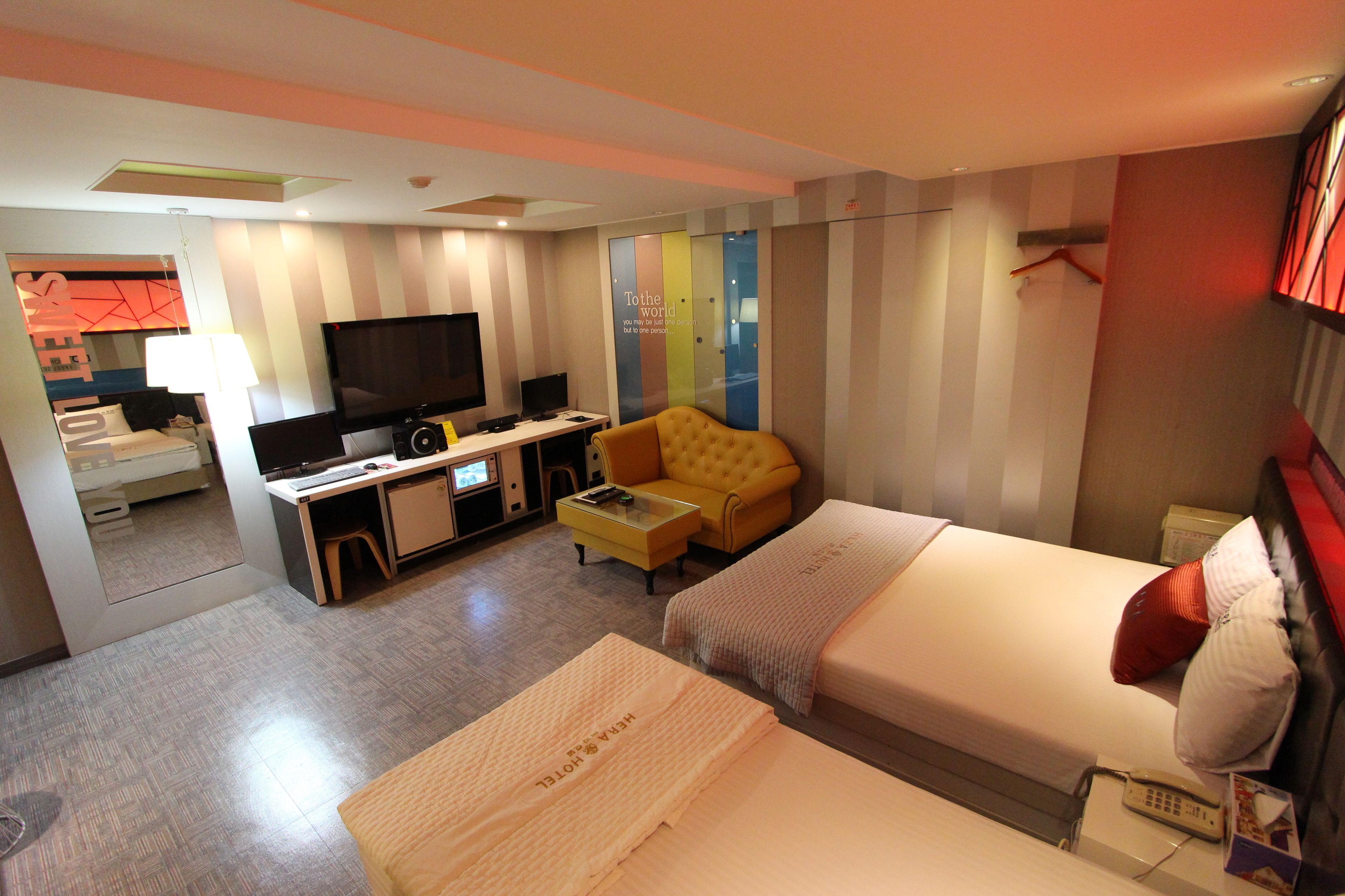 A hotel room with a bed, a sofa, a desk with a TV, and a small table.