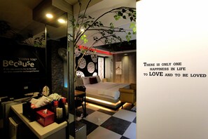 A hotel room with a checkered floor, a bed with a white comforter, a bedside table with a lamp, and a wall with a quote about love.