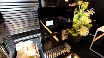 Una máquina de café con pantalla digital, una bandeja de vasos desechables y una planta en maceta con flores.