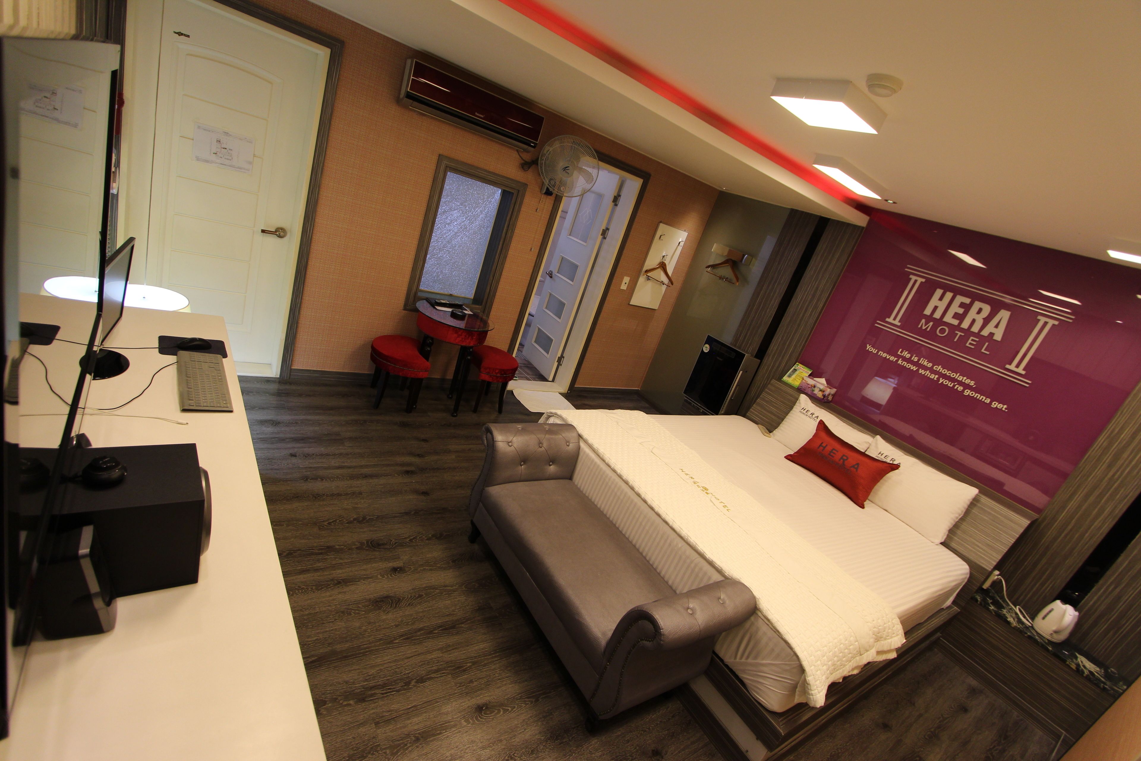 A hotel room with a bed, a desk with a computer, a chair, and a small table.