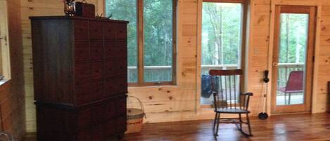 A wooden cabin interior with a large wooden dresser, a rocking chair, and a rug on the floor.