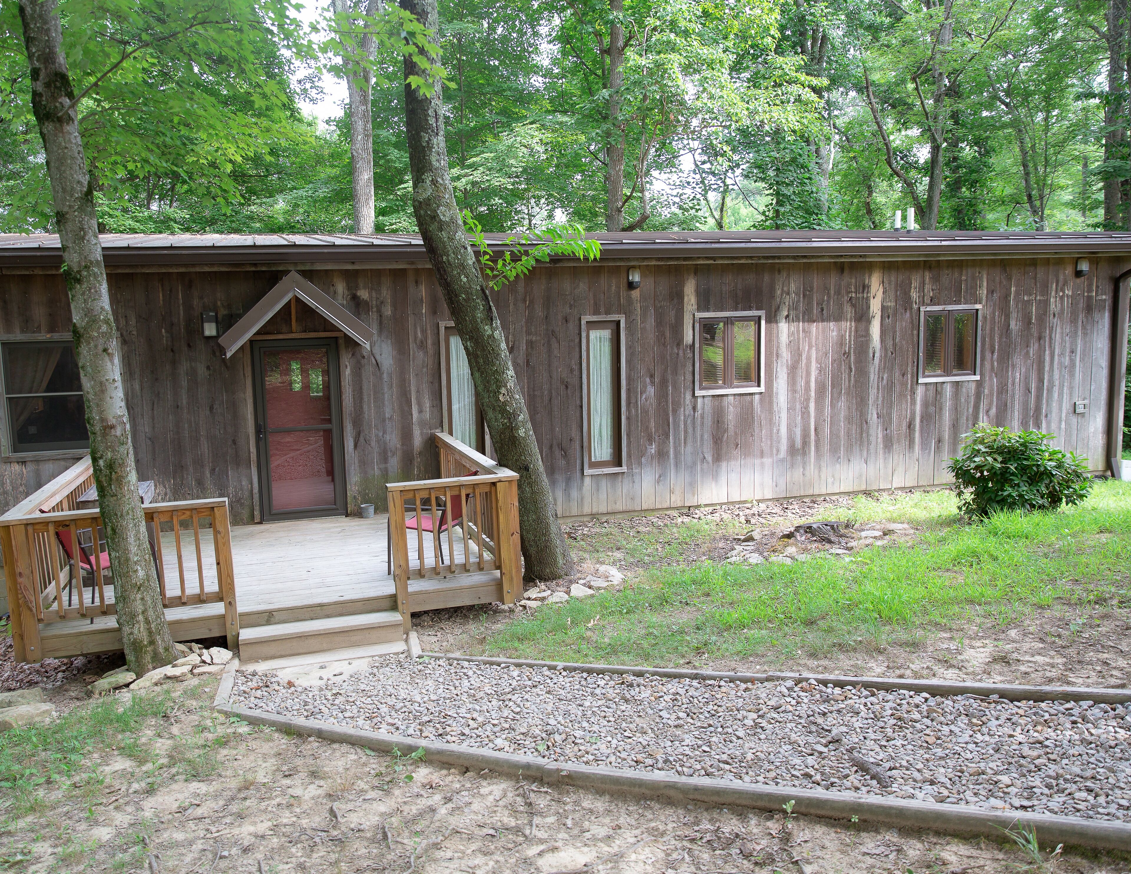 A rustic wooden cabin with a porch, a small garden, and a gravel pathway.