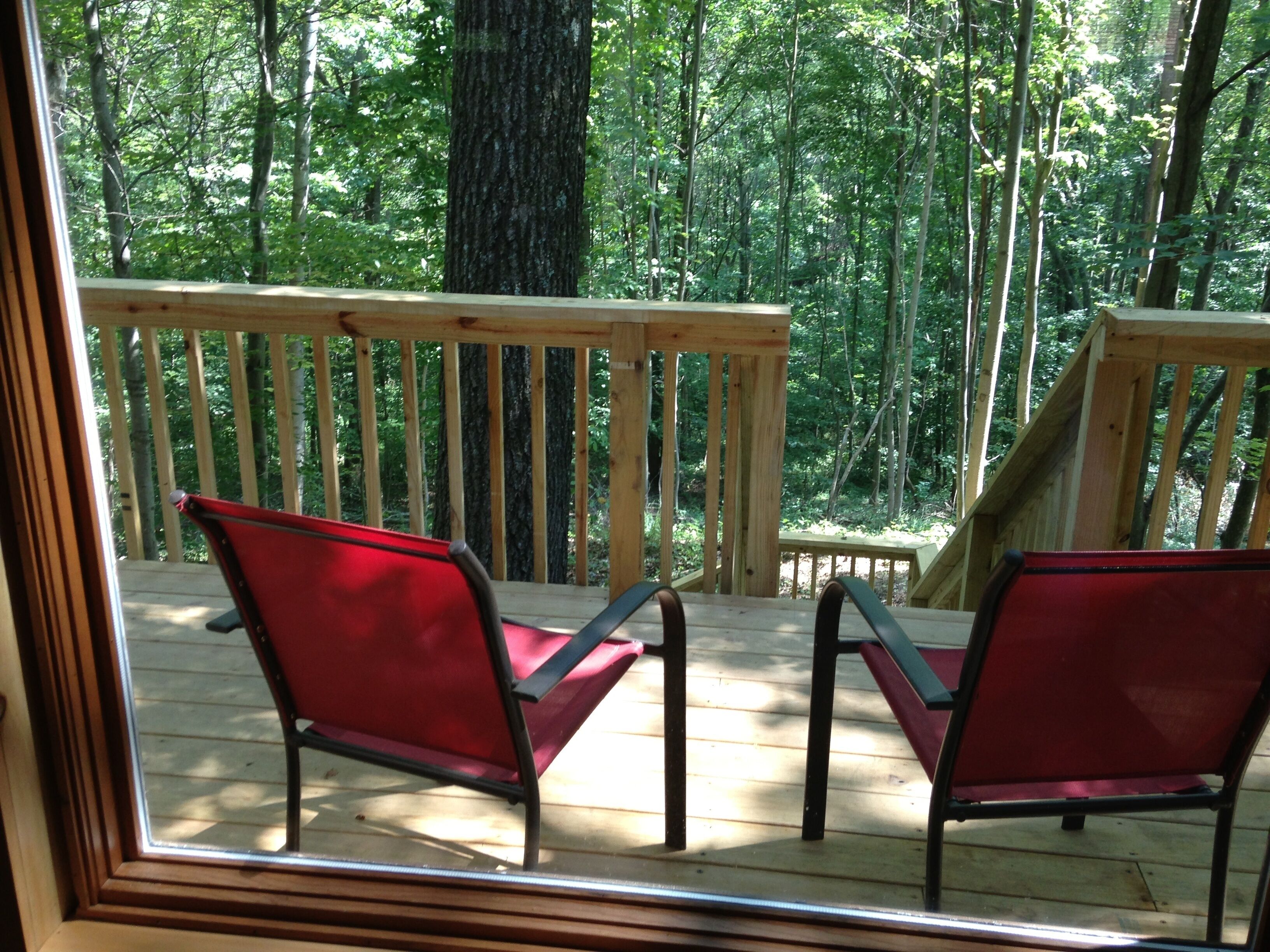 Een houten terras met twee rode stoelen en een houten leuning.