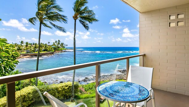 A balcony with a view of the ocean, palm trees, and a tiled table. - A Beautiful Condo at the Waters Edge with a Great View (Koloa)