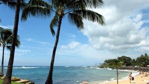 A beach with palm trees, ocean waves, and a clear sky. - A Beautiful Condo at the Waters Edge with a Great View (Koloa)