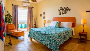 Habitación de hotel con cama, una silla, una mesita, una lámpara y vista al mar por la ventana.