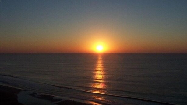 A sunset over the ocean with calm waters reflecting the sun's light.
