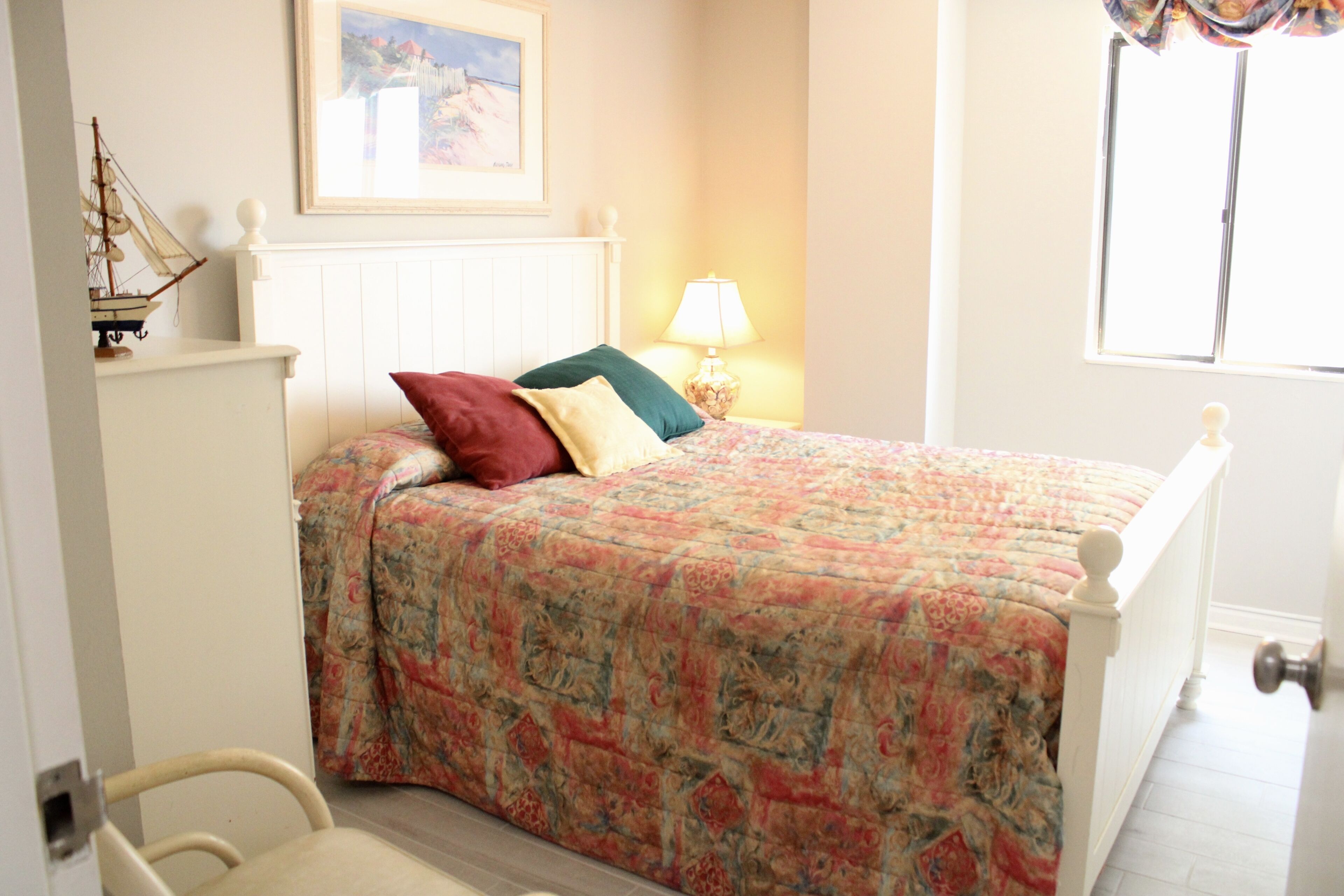 A bedroom with a bed, a nightstand with a lamp, a chair, and a window with curtains.