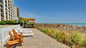 A beachfront patio with lounge chairs and a pergola, overlooking the ocean.