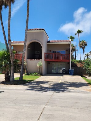 A two-story building with a red balcony, a garage door, and a clear sky.