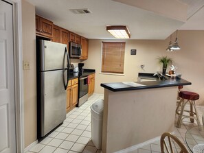 A kitchen with wooden cabinets, a stainless steel refrigerator, a microwave, a stove, and a sink.