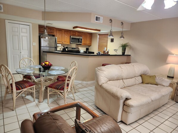A compact living space with a kitchenette, a dining area with a glass table, and a sofa.