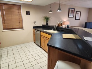 A kitchen with wooden cabinets, a black countertop, a dishwasher, and a sink.