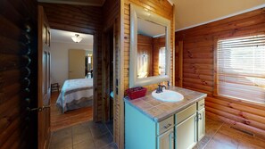 Interior de una cabaña de madera con baño que incluye lavamanos, espejo y armarios.