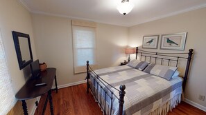 A bedroom with a bed, a desk, a chair, a lamp, and two framed pictures on the wall.