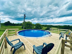 Una terraza de madera con piscina, rodeada de sillas y un cerco de madera.