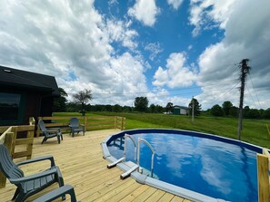 A wooden deck with a swimming pool, surrounded by a wooden fence and chairs.
