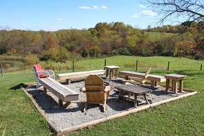 An outdoor seating area with wooden benches and chairs, surrounded by a gravel path and grass.