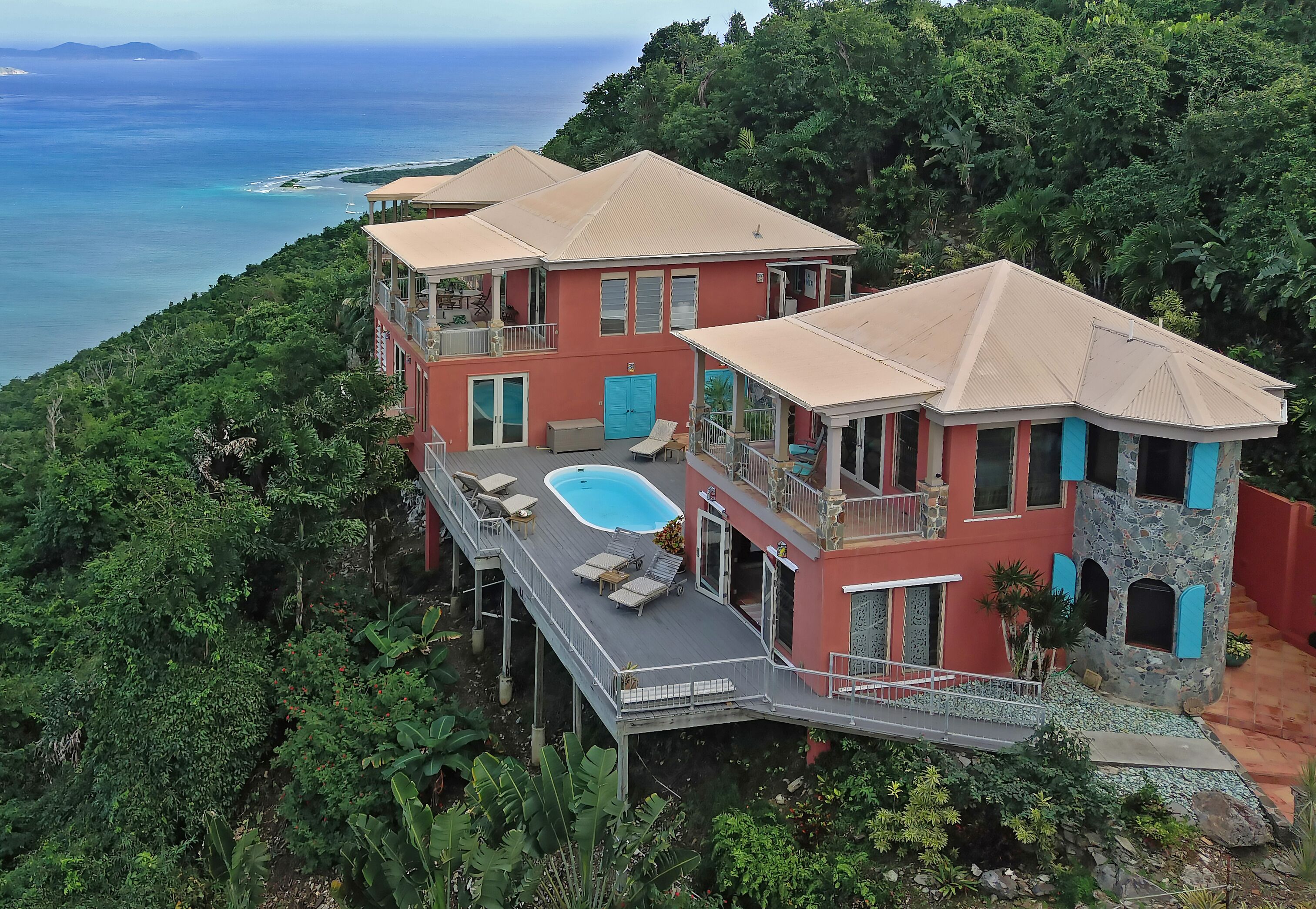 Ein mehrstöckiges Haus mit Schwimmbad, umgeben von üppiger Vegetation und mit Blick auf einen Strand.
