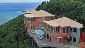 Ein mehrstöckiges Haus mit Schwimmbad, umgeben von üppiger Vegetation und mit Blick auf einen Strand.