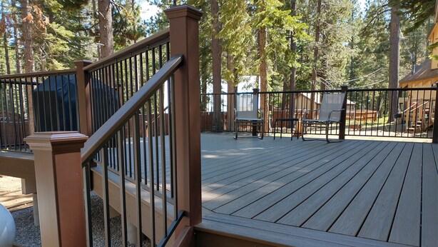 A wooden deck with a metal railing, surrounded by trees. - All The Comfort Of Home <br> Permit Number 0498 (South Lake Tahoe)