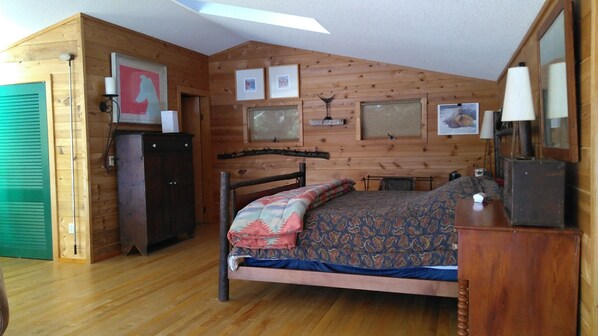 Una habitación con paneles de madera, una cama, un aparador y un espejo. Hay cuadros en la pared y una puerta verde.