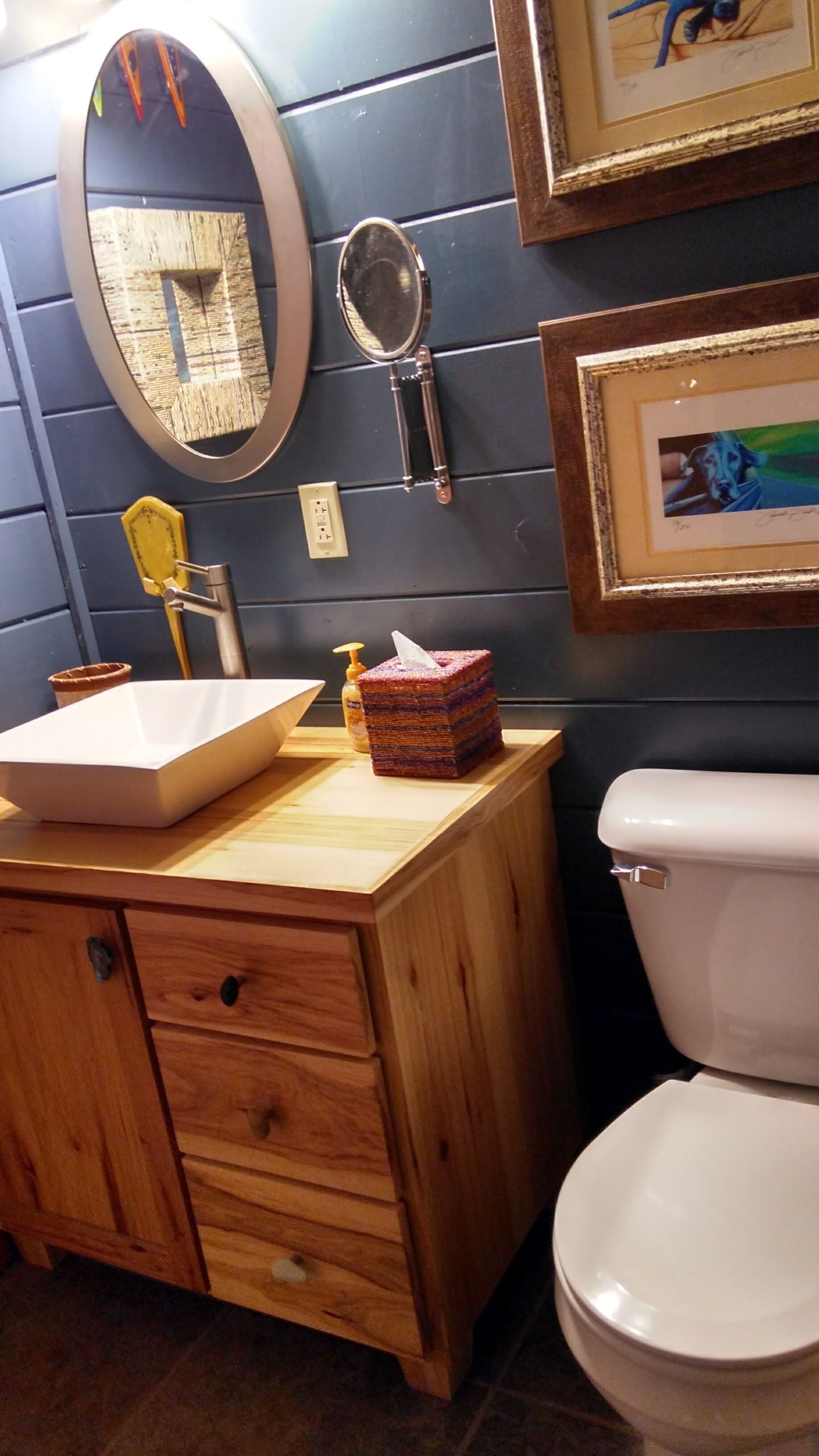 A bathroom with a wooden vanity, a sink, a mirror, a framed picture, and a toilet.
