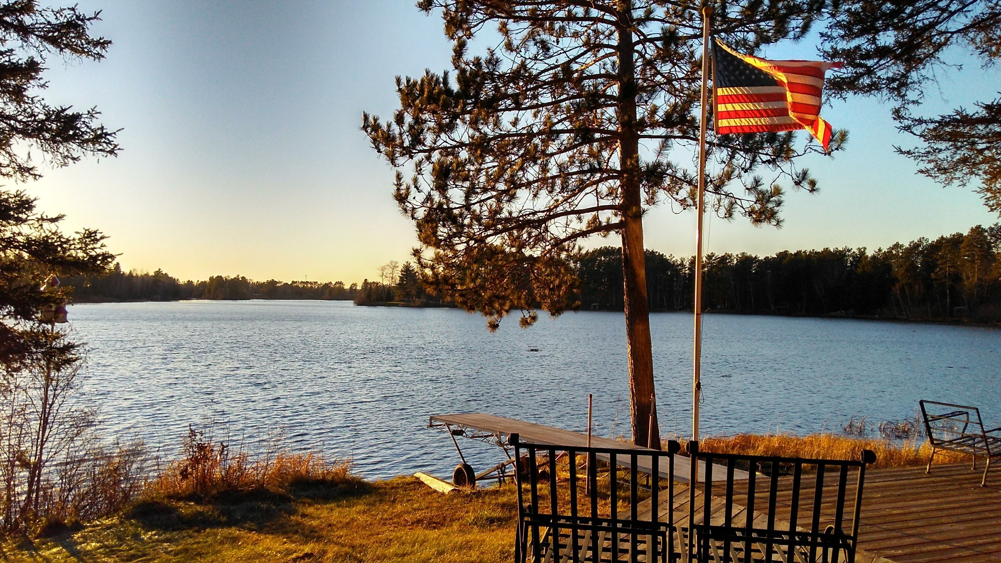 Une vue sur le lac avec un quai, un drapeau et un banc.