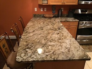 Una cocina con encimera de granito, sillas de madera, estufa y armarios.