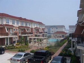 Un edificio residencial con varios balcones, una piscina y un aparcamiento con coches.
