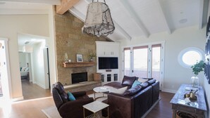 A spacious living room with a stone fireplace, leather sofas, and a television. - Playa Penthouse (Ocean Views) (Carpinteria)