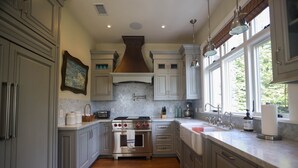 A kitchen with gray cabinets, a stainless steel stove, and a window providing natural light. - Playa Penthouse (Ocean Views) (Carpinteria)