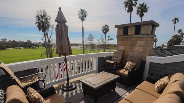 A balcony with outdoor furniture, a stone fireplace, and a view of a golf course. - Playa Penthouse (Ocean Views) (Carpinteria)
