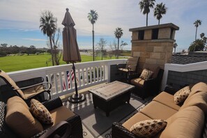 A balcony with outdoor furniture, a stone fireplace, and a view of a golf course.