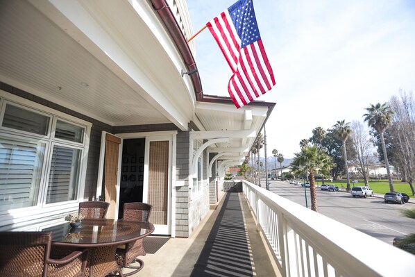 Ein überdachter Außenbereich mit Tisch und Stühlen, einer US-amerikanischen Flagge und Blick auf eine Straße mit Autos und Palmen.