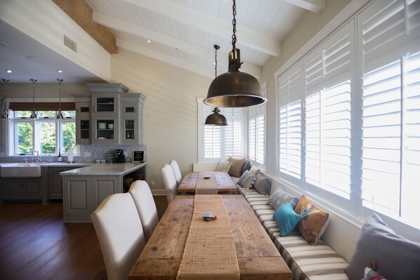 A spacious kitchen with a dining area, large windows, and a hanging light fixture.