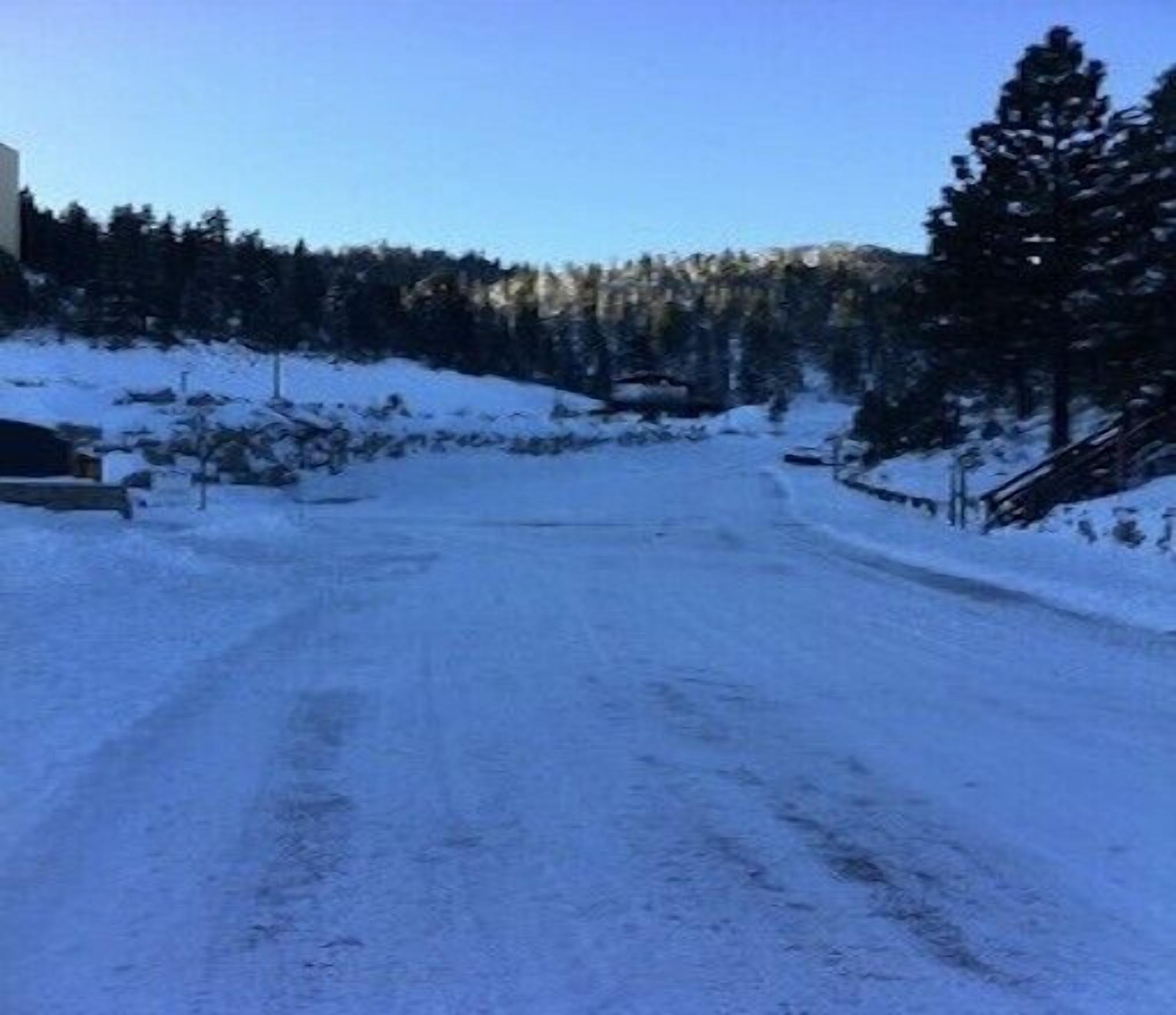 A snow-covered road with a wooden bridge and dense forest in the background.